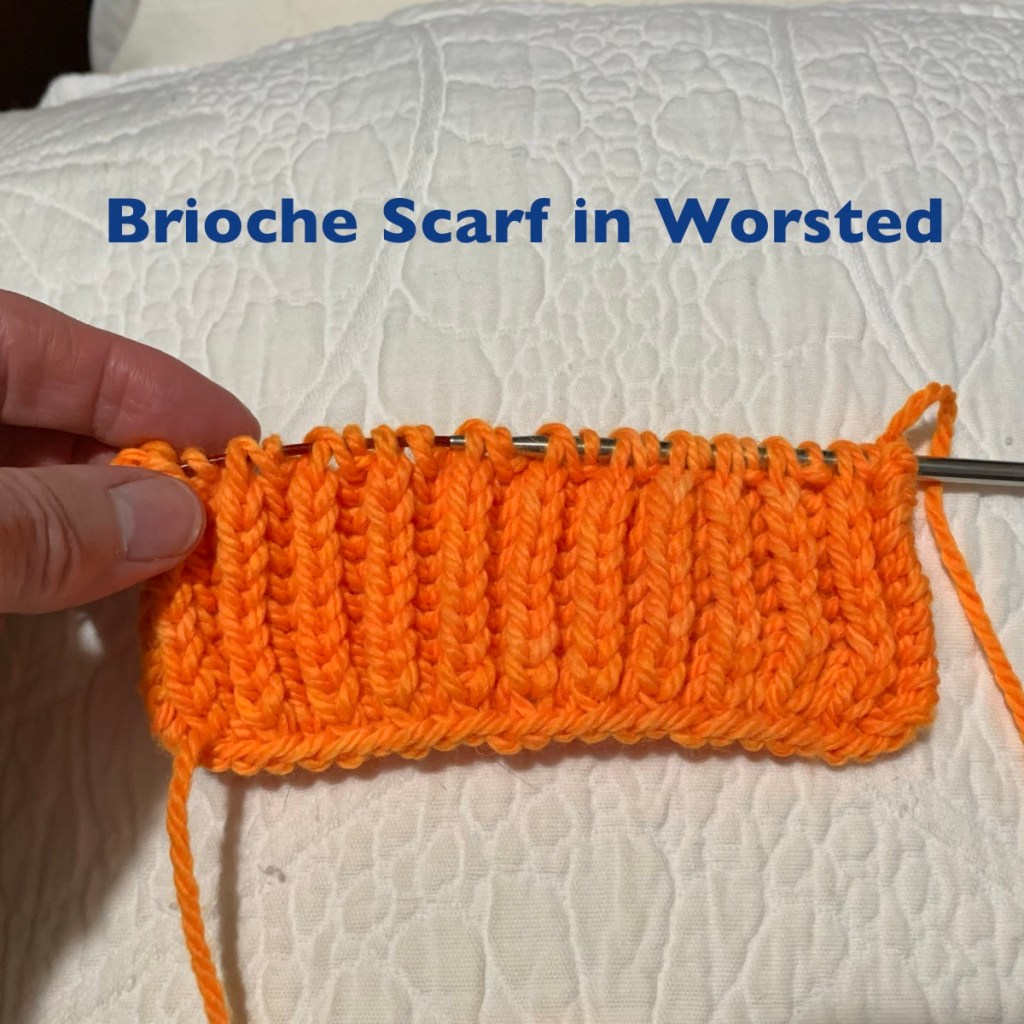 Close-up of an orange brioche scarf being knitted with a knitting needle, resting on a textured white surface.