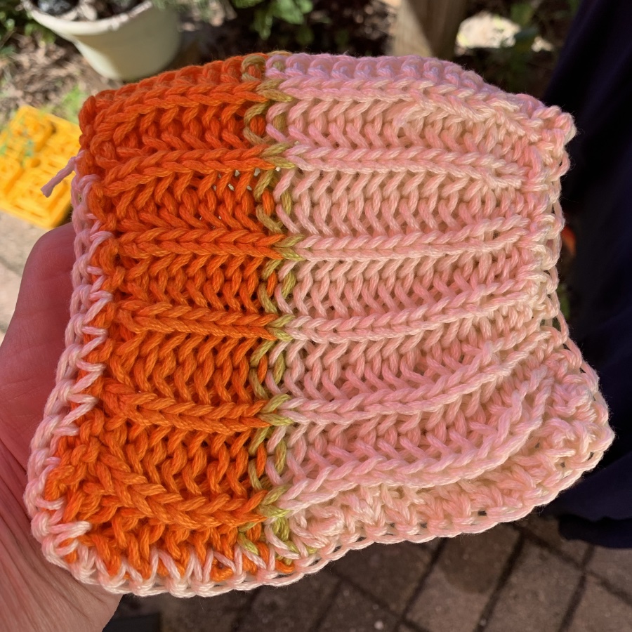 A handmade crochet piece featuring a gradient of orange and pink hues, with distinct textured patterns.